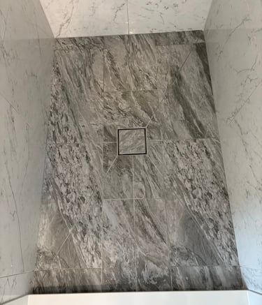 Modern bathroom shower featuring envelope cut floor tiles and a square center tile in drain.
