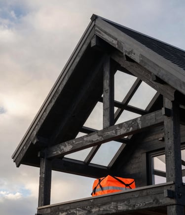 Detailed architectural photography of a perfectly finished roof structure of a modern Northern European / Finnish villa. High contrast with Soft Off-White clouds in the background, Dark Slate Black structural beams, and a glimpse of Vibrant Safety Orange safety equipment. Premium feel, sharp focus.