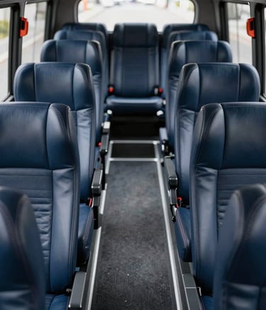 A high-angle interior shot of a modern luxury bus, showcasing deep navy leather seats with integrated headrests and a clean, spacious aisle. The lighting is bright and professional, highlighting a sophisticated and reliable travel environment in a North American setting.