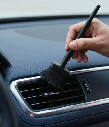 A close-up, high-angle shot of a detailer's hands using a soft-bristled brush to meticulously clean the intricate vents of a luxury car dashboard. The lighting is bright and professional, highlighting the texture of the high-quality materials. The color palette features deep blues and clean metallic accents, embodying a sense of professional care.