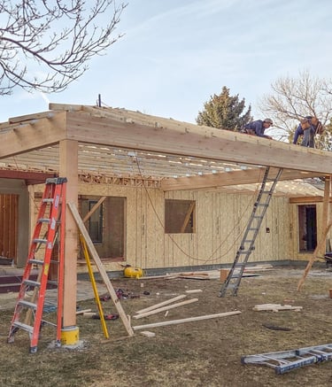 Framing progressing on a new home addition, showing wall sheathing and roof trusses by Elk Valley Contractors.