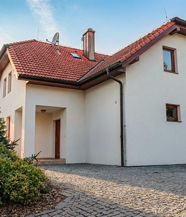 Modern white two-story house with a red tiled roof and cobblestone driveway at sunset.