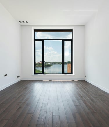Empty modern room with dark hardwood floors and a large window overlooking a scenic lake.