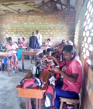 Students in a vocational training center learning tailoring and sewing skills using manual machines.