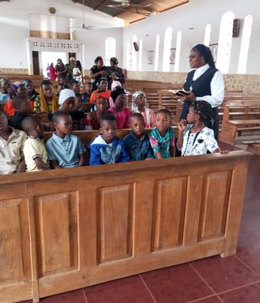 A Catholic nun teaching children sitting in wooden pews inside a church during a religious lesson.