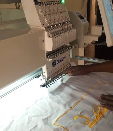 A professional operator using an industrial Disen computerized embroidery machine to stitch yellow designs on white fabric.