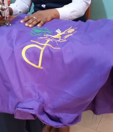 A tailor using a vintage sewing machine to embroider a gold religious symbol on purple fabric.