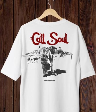 Camisa blanca con gráfico “Call Soul” y estampado de camello del desierto, colgada en pared madera.