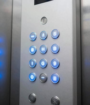 A detailed close-up shot of a modern elevator control panel with glowing buttons, located inside a corporate building in Maputo, Mozambique. The lighting highlights the Mist White and Soft Blue tones, reflecting a professional and innovative atmosphere.