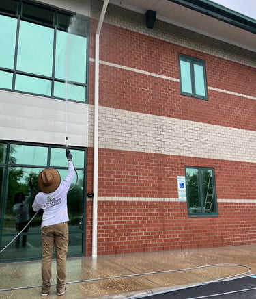 Professional soft wash technician cleaning a commercial brick building and windows with a pressure washer.