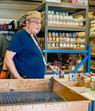 Volunteer man standing in food pantry with canned food in background