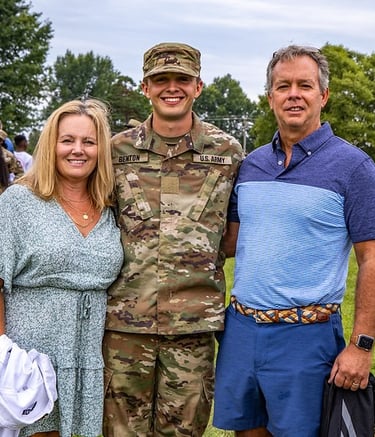 Two parents standing with their son who is in Army camoflage.  They are with other families.