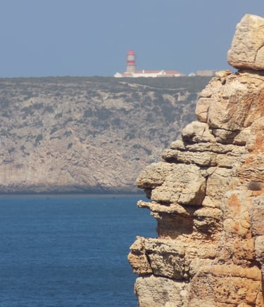 roccia in primo piano con sfondo di oceano e faro che si scorge in lontananza.