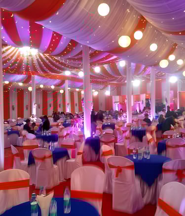 "Large indoor event space decorated with red and white drapes, hanging lights, round tables.