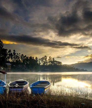 Tiga perahu bersandar di tepi Danau Situ Cileunca saat matahari terbit, dengan kabut tipis dan pantulan langit di permukaan a