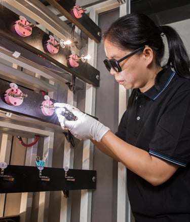 A technician wearing safety glasses inspects bright automotive light bulbs on a testing rack.