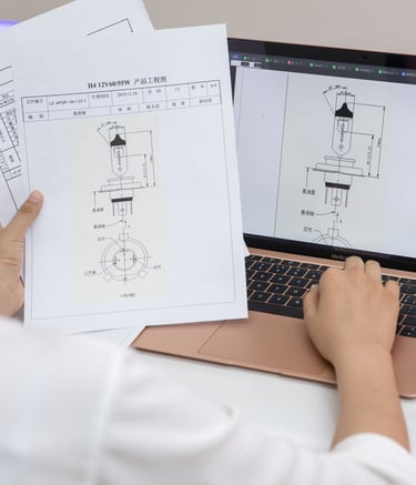 Engineer reviewing H4 halogen headlight bulb technical blueprints on a laptop and paper.