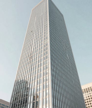 A sharp, low-angle shot of a modern glass skyscraper in a North American business district against a clear sky, utilizing a color palette of soft white and pale blue gray for a professional and minimalist feel.