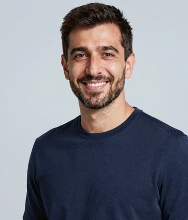 A high-quality, professional portrait of Mustafa ORAN in a minimalist setting. He wears a smart-casual outfit in #1A2C3D navy. The background is a soft #BCCAD6 light blue-gray. The lighting is warm and welcoming, capturing a friendly and trustworthy expression.