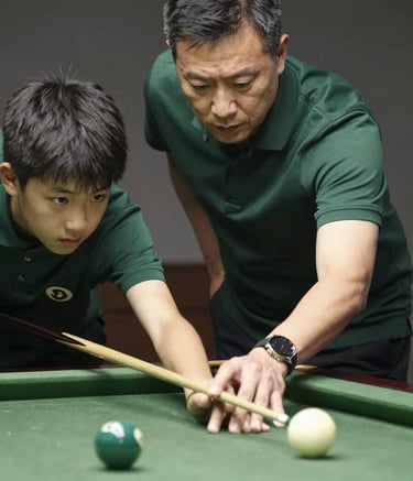 A focused close-up photograph of an adult mentor in a dark forest green polo shirt guiding a teenager on how to hold a billiards cue properly. The lighting is soft and natural, emphasizing a teaching moment in a professional environment. The pool table felt is a clean, muted sage green.