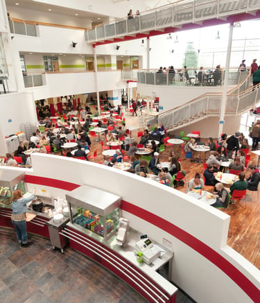 Students dining in a busy multi-level modern university cafeteria and student union hub.