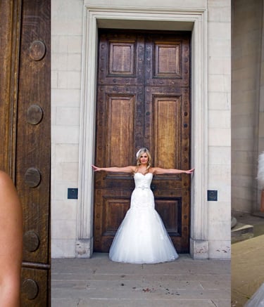 A smiling bride in a lace wedding dress and birdcage veil poses by wooden doors and with her groom in a kilt.