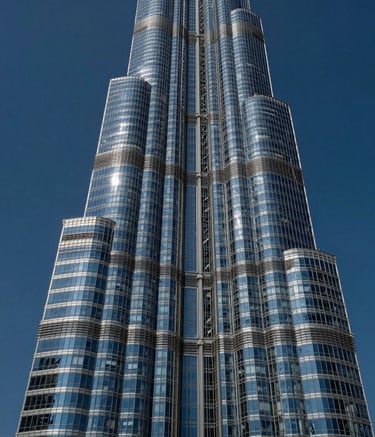 A high-contrast architectural photograph of a modern skyscraper in the UAE against a deep blue sky. The building's glass facade reflects the sophisticated urban environment of the Gulf.