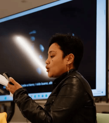 una mujer negra con jaqueta de cuero sujetando un papel y un móvil