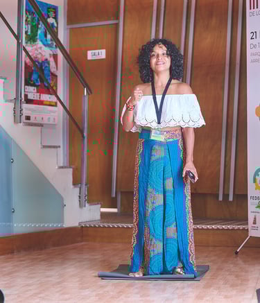 una mujer afrodescendiente con top blanco y falda larga azul hablando en un escenario