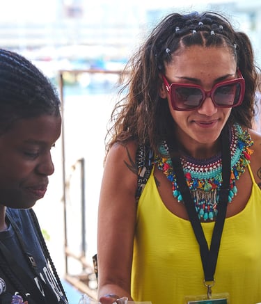 Una mujer afro al lado de otra con vestido amarillo gafas de sol y collar afro grande