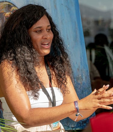 una mujer afro con un top blanco hablando delante de un cuadro