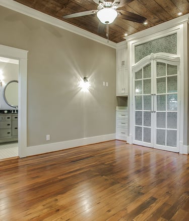 Elegant room with reclaimed wood floors, a ceiling fan, and white built-in cabinets near a bathroom.