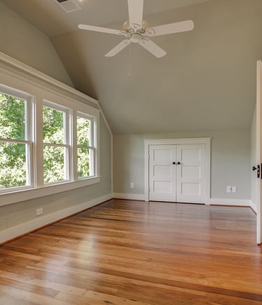 Empty modern attic bedroom with hardwood floors, exposed brick chimney, and large windows.