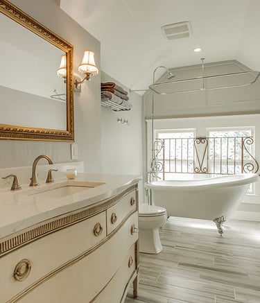 Elegant master bathroom with a vintage vanity, gold framed mirror, and clawfoot soaking tub.