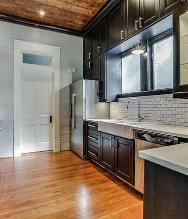 Modern kitchen with dark cabinets, white subway tile backsplash, and rustic wood ceiling.
