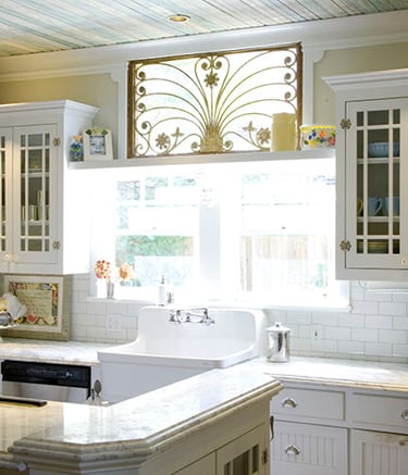 Vintage white kitchen featuring a farmhouse sink, subway tile backsplash, and ornate gold window gate.