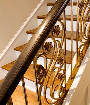 Elegant oak wood staircase featuring an ornate gold wrought iron railing with floral scrollwork.