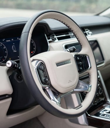 A close-up photograph of a luxury SUV's polished dashboard and leather-wrapped steering wheel. The lighting is soft and natural, highlighting the pristine condition of the interior. Accents of Slate Steel Blue and Mist White are visible in the digital display and reflections, conveying modern professionalism.