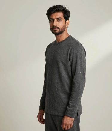 A professional, ultra-minimalist portrait of M. Moiz Maqsood in a North American architecture studio setting. The subject is wearing charcoal grey attire, looking confidently off-camera. The background is a clean off-white wall with soft, natural side lighting and generous negative space.