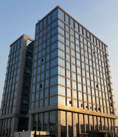 A high-impact photo of the AdiShakti Enterprises headquarters in Gujarat, featuring modern corporate architecture with slate blue glass panels and golden morning light. Global B2B / Indian Origin setting.