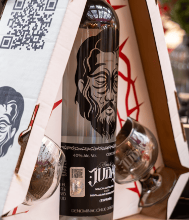 A bottle of Alma de Judas artisanal mezcal espadin with two tasting glasses in a branded display box.