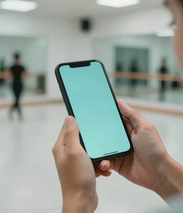 A close-up of a person's hands holding a smartphone in a modern Spanish / Latin American dance studio. The background is softly blurred showing a clean dance floor and mirrors, with a palette of Soft Aqua and Pale Mist.