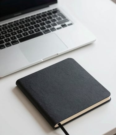 Close-up of a professional desk with a high-end laptop and a minimalist black notebook, muted color palette of light gray and dark charcoal, North American business setting, bright natural light.
