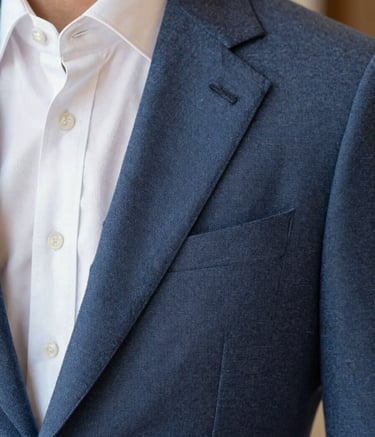 A close-up shot focusing on the high-quality texture of a slate blue wool suit and a crisp pearl white shirt. The composition is artistic and modern, emphasizing detail and professionalism in the Brazilian menswear industry.