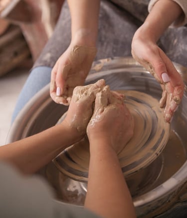 Manos dando forma a una vasija de barro en un torno de alfarería durante una clase de cerámica.