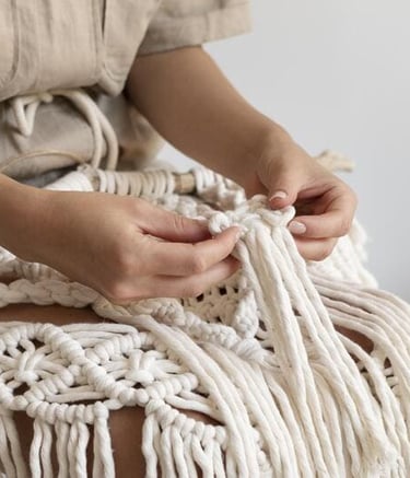 Primer plano de manos elaborando un tapiz de macramé DIY con cordón de algodón blanco y nudos boho.