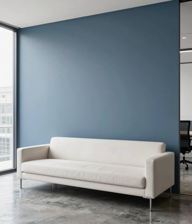 A high-end, minimalist office interior in the US. A sleek slate blue wall serves as a backdrop for an off-white modern sofa. The floor is polished concrete. Natural light pours in from a large window.
