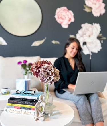 Woman sitting on a couch typing on a laptop with a stack of books nearby