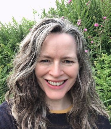 smiling woman with greying hair standing before wild flowers