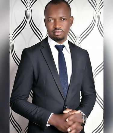 Professional portrait of a man wearing a black business suit and blue tie against a patterned background.